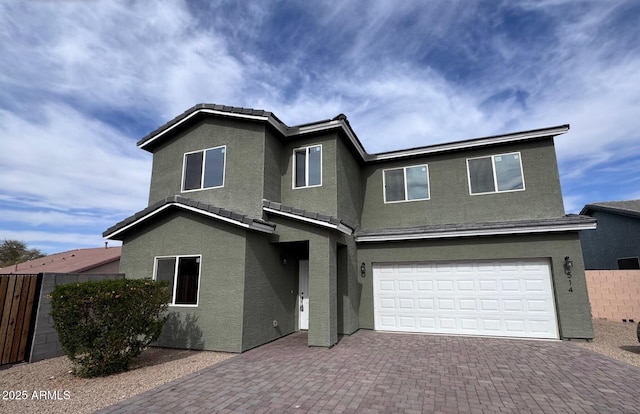 view of front facade with a garage, a tiled roof, fence, decorative driveway, and stucco siding