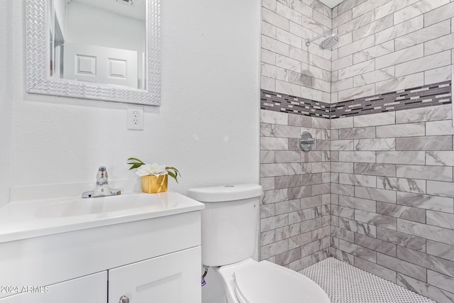 bathroom featuring a tile shower, vanity, and toilet