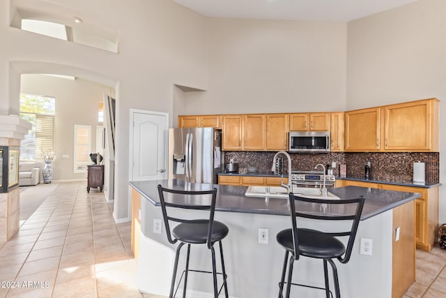 kitchen featuring high vaulted ceiling, light tile patterned flooring, stainless steel appliances, and a kitchen island with sink