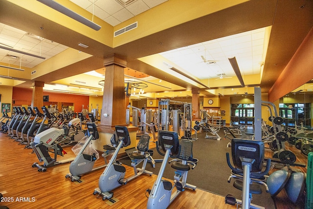 workout area featuring a paneled ceiling, wood finished floors, visible vents, and ornate columns