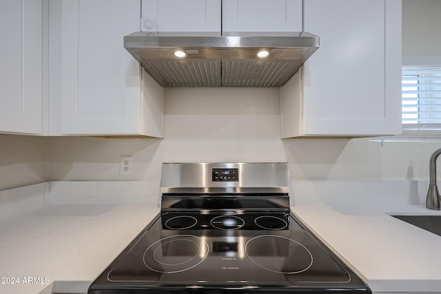 kitchen with sink, stainless steel stove, light stone counters, range hood, and white cabinets