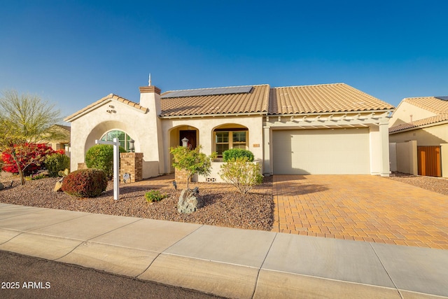 mediterranean / spanish house with decorative driveway, stucco siding, an attached garage, roof mounted solar panels, and a tiled roof