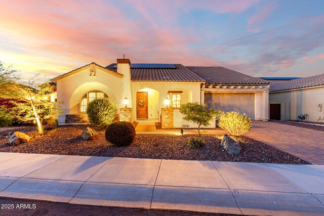 18322 W Thistle Landing Dr, Goodyear, AZ 85338 - mediterranean / spanish house featuring driveway, a tiled roof, solar panels, stucco siding, and a garage