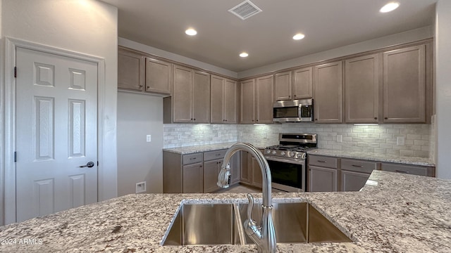 kitchen featuring appliances with stainless steel finishes, tasteful backsplash, light stone counters, and sink