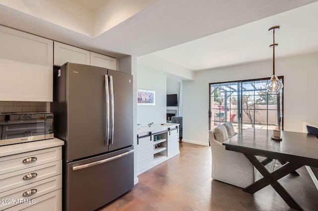 kitchen with pendant lighting, light countertops, backsplash, freestanding refrigerator, and white cabinets