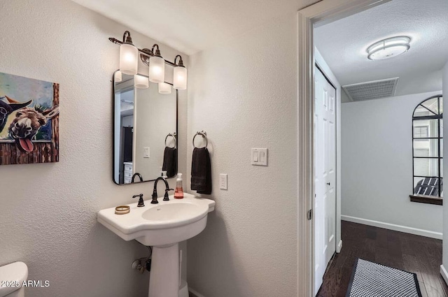 bathroom featuring a textured ceiling, a textured wall, wood finished floors, visible vents, and baseboards