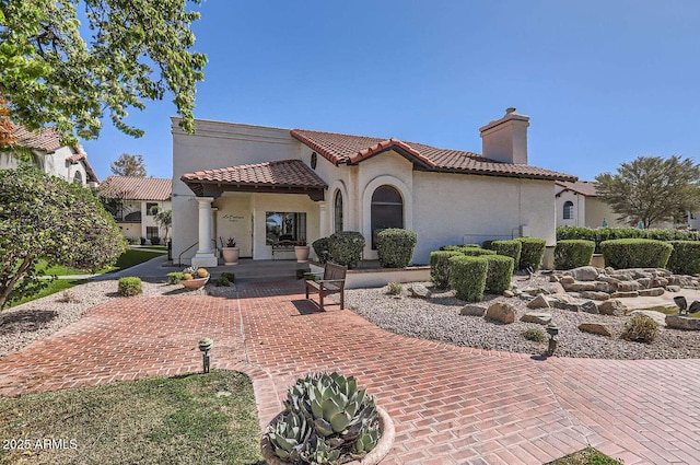 mediterranean / spanish-style house with a chimney, a tile roof, and stucco siding