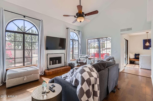 living room with a fireplace with raised hearth, high vaulted ceiling, wood-type flooring, and visible vents