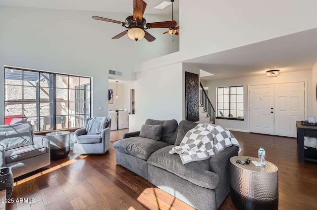 living room featuring dark wood-type flooring, stairway, a towering ceiling, and visible vents