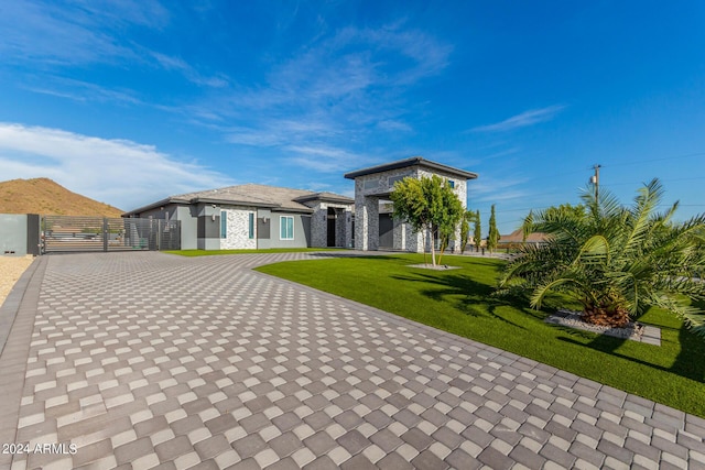 prairie-style home with a front lawn, a gate, decorative driveway, and stone siding