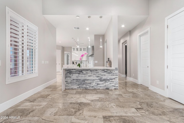 kitchen with baseboards, visible vents, hanging light fixtures, white cabinetry, and wall chimney range hood