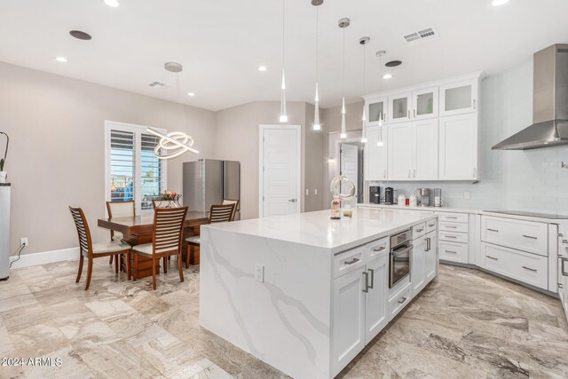 kitchen with oven, white cabinetry, a center island with sink, and wall chimney range hood