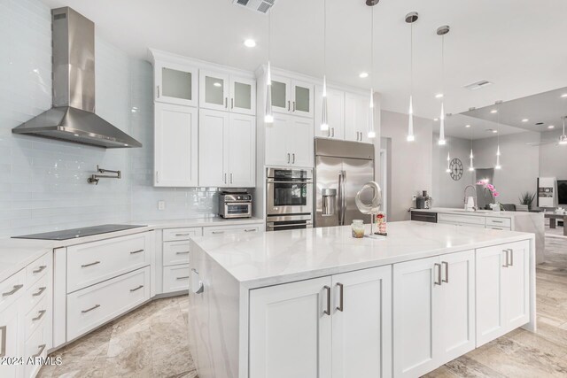 kitchen with white cabinetry, wall chimney range hood, light stone counters, stainless steel appliances, and decorative backsplash