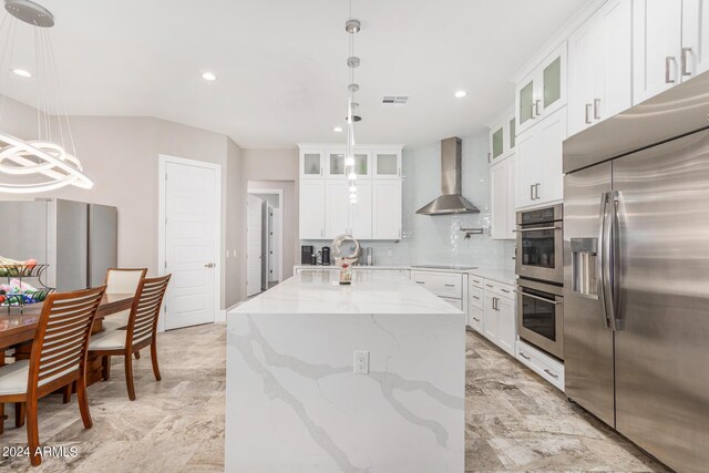 kitchen with white cabinets, stainless steel appliances, light stone countertops, wall chimney exhaust hood, and decorative light fixtures