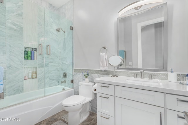 bathroom featuring toilet, combined bath / shower with glass door, tile walls, wainscoting, and vanity