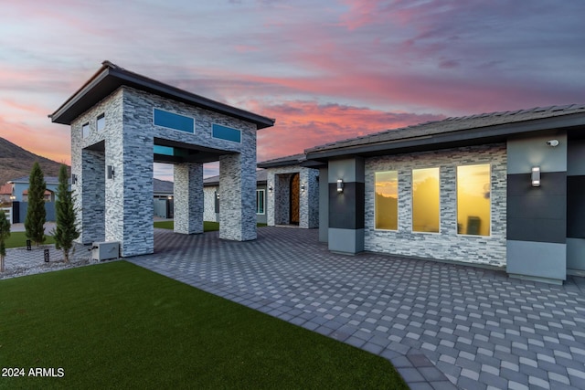 rear view of property featuring a patio area, stone siding, stucco siding, and a yard