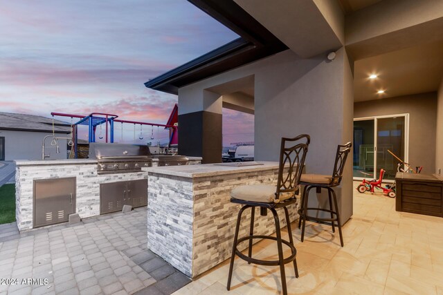 patio terrace at dusk featuring an outdoor kitchen, a grill, and an outdoor bar