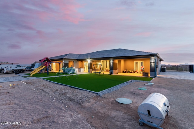 back of house at dusk featuring stucco siding, a lawn, a playground, and fence