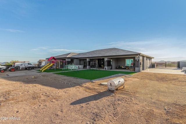 view of front of house featuring a front lawn, a playground, fence, and stucco siding