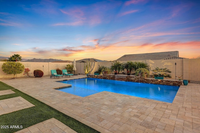 pool at dusk featuring pool water feature and a patio area