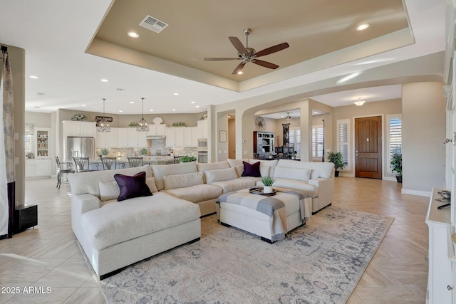 living room with ceiling fan with notable chandelier and a tray ceiling