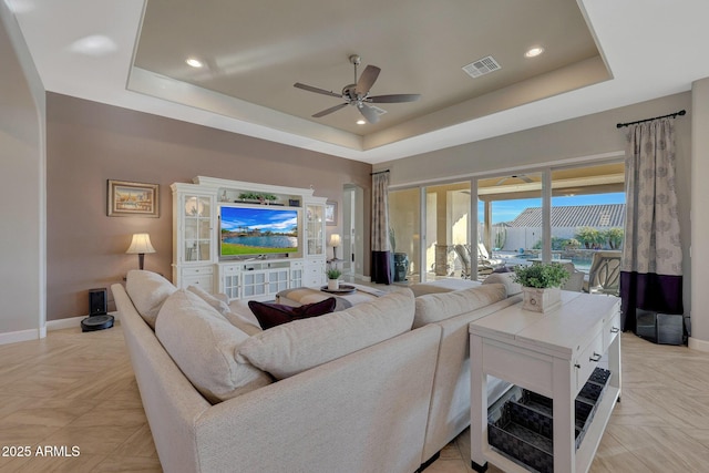 living room featuring light parquet floors, a raised ceiling, and ceiling fan