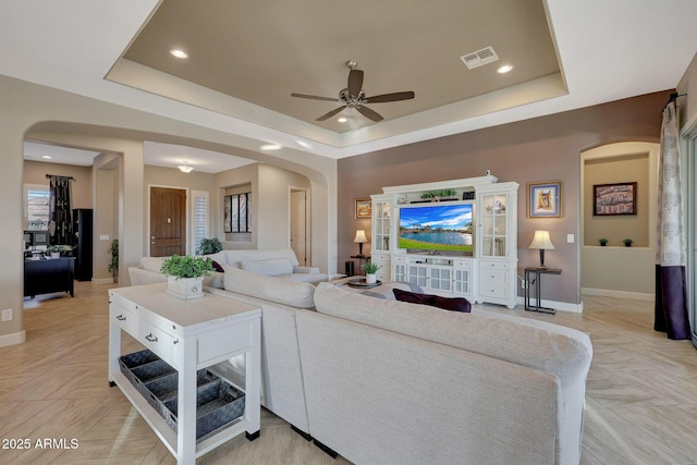 living room with a tray ceiling, light parquet flooring, and ceiling fan