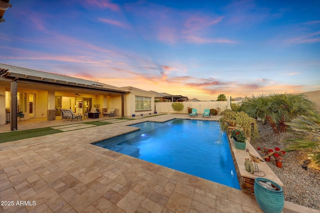 pool at dusk featuring pool water feature and a patio area