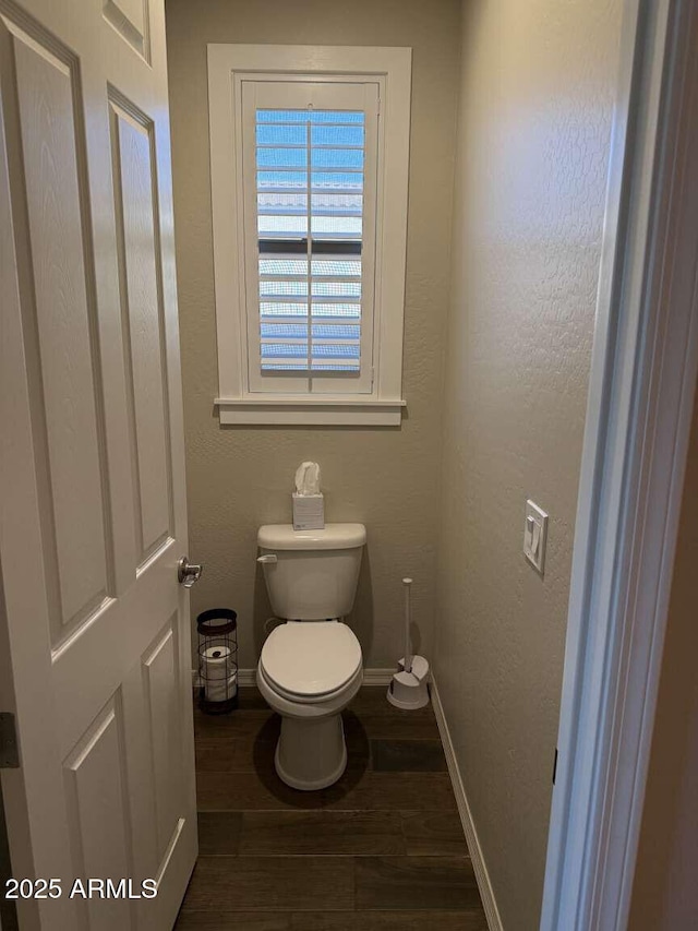 bathroom featuring toilet, wood finished floors, baseboards, and a textured wall