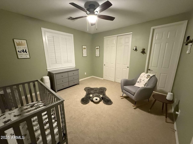 bedroom with a crib, ceiling fan, baseboards, carpet flooring, and a closet