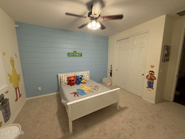 bedroom featuring visible vents, wood walls, light carpet, a closet, and a ceiling fan