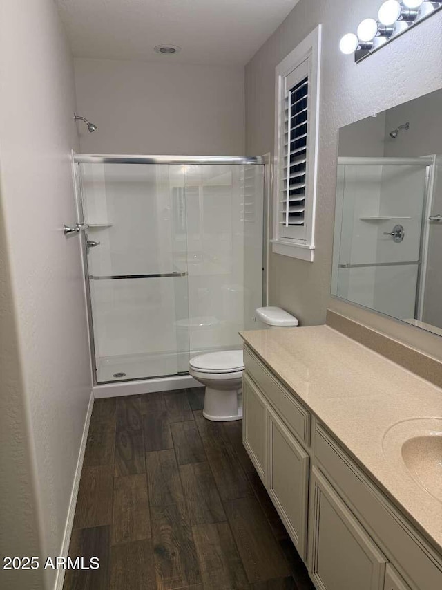 bathroom with a stall shower, toilet, baseboards, and wood finished floors