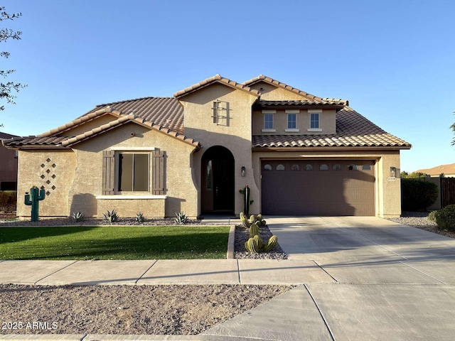 mediterranean / spanish home featuring stucco siding, a front lawn, concrete driveway, a garage, and a tiled roof