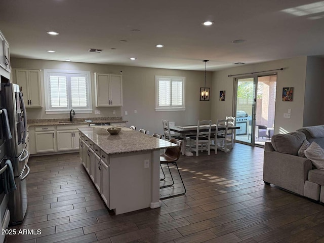 kitchen with a kitchen island, dark wood-style flooring, a sink, white cabinetry, and open floor plan