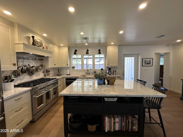 kitchen with white cabinetry, double oven range, a center island, and a kitchen bar