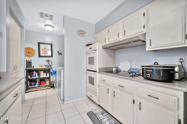 kitchen with black electric stovetop, white double oven, white cabinetry, and light tile patterned floors