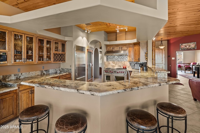 kitchen with wood ceiling, high end appliances, backsplash, kitchen peninsula, and a breakfast bar