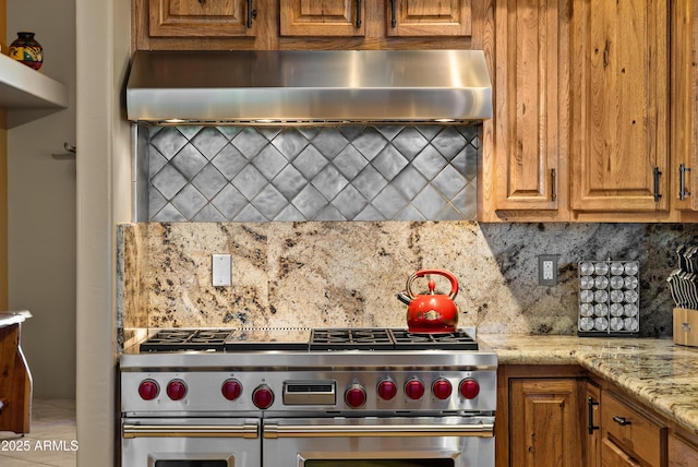 kitchen featuring decorative backsplash, double oven range, light stone counters, and ventilation hood