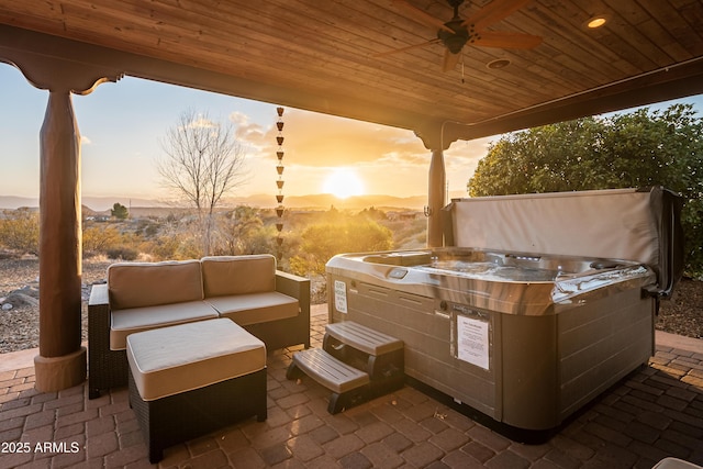 patio terrace at dusk with ceiling fan, an outdoor hangout area, and a hot tub