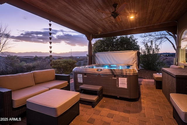 patio terrace at dusk featuring ceiling fan, a hot tub, and an outdoor living space