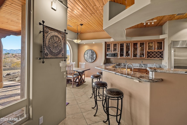 kitchen featuring wooden ceiling, light tile patterned flooring, light stone countertops, pendant lighting, and built in appliances