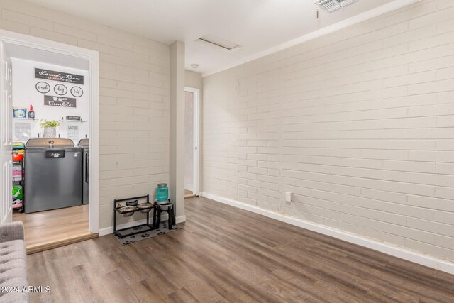 unfurnished living room featuring hardwood / wood-style floors, washer and clothes dryer, and brick wall