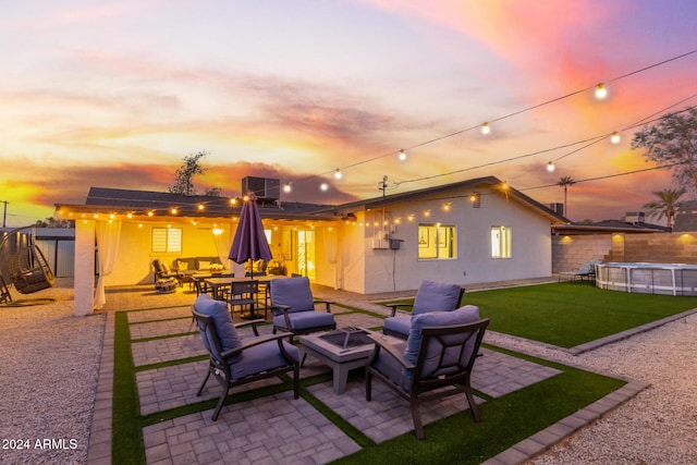 back house at dusk with a lawn, a patio area, and an outdoor living space with a fire pit