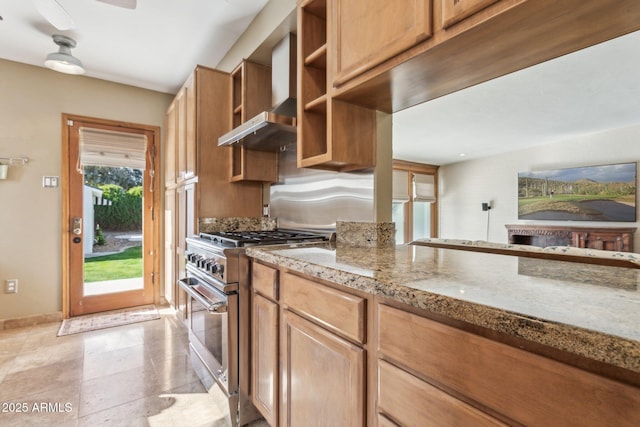 kitchen with baseboards, a ceiling fan, wall chimney exhaust hood, light stone countertops, and high end stove