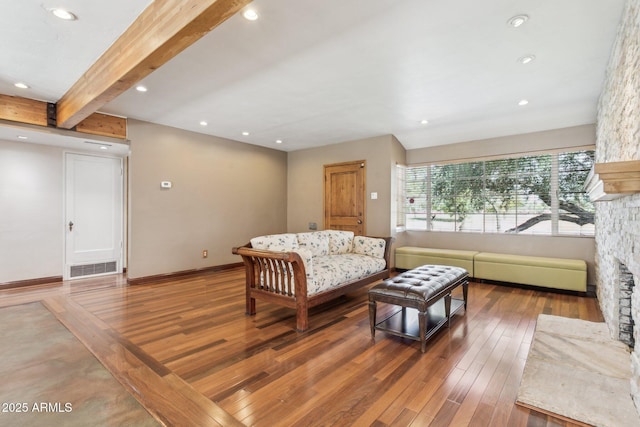 living room featuring a fireplace, visible vents, beamed ceiling, baseboards, and hardwood / wood-style flooring