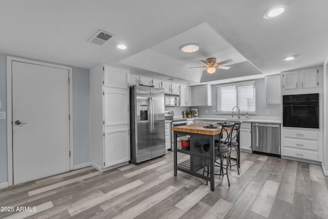 kitchen featuring visible vents, a tray ceiling, stainless steel appliances, light countertops, and a sink