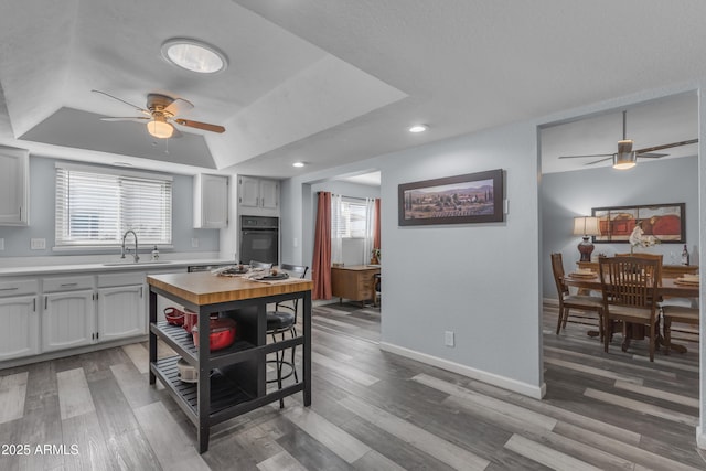 kitchen with light countertops, a raised ceiling, black oven, and wood finished floors