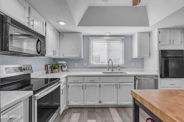 kitchen featuring light wood finished floors, a raised ceiling, white cabinets, a sink, and black appliances