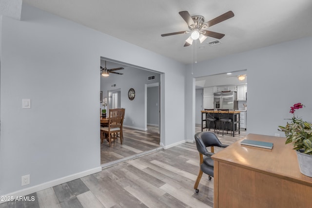 office space featuring baseboards, a ceiling fan, visible vents, and light wood-style floors