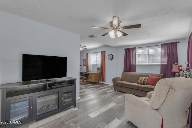 living room with baseboards, wood finished floors, visible vents, and a ceiling fan